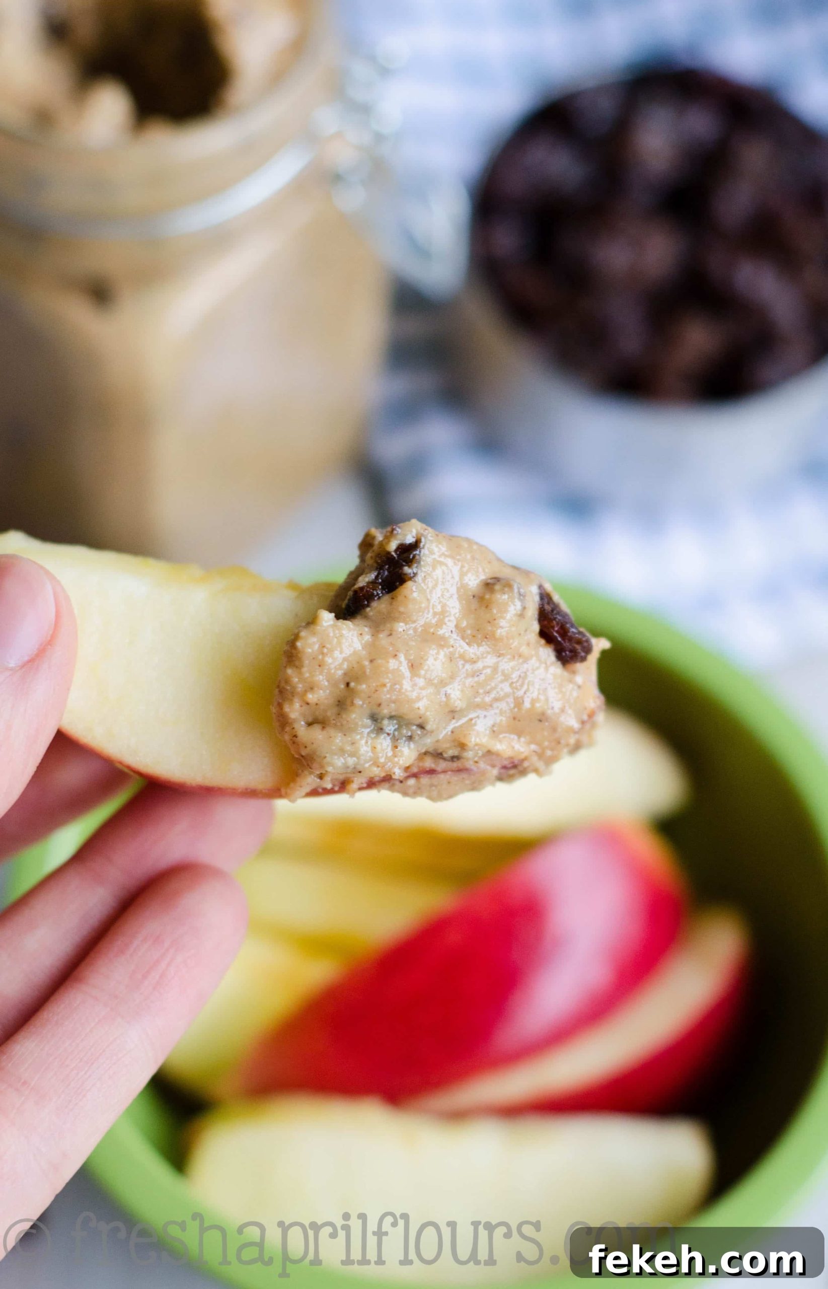 Hand holding an apple slice with cinnamon raisin peanut butter spread on it.