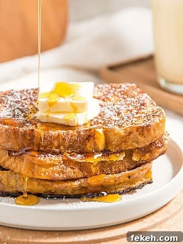 Three slices of French toast with butter and dripping syrup. White plate, Light wood background.