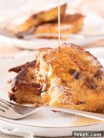 Syrup drizzle on two slices of French toast with panettone on a white plate with a silver fork.