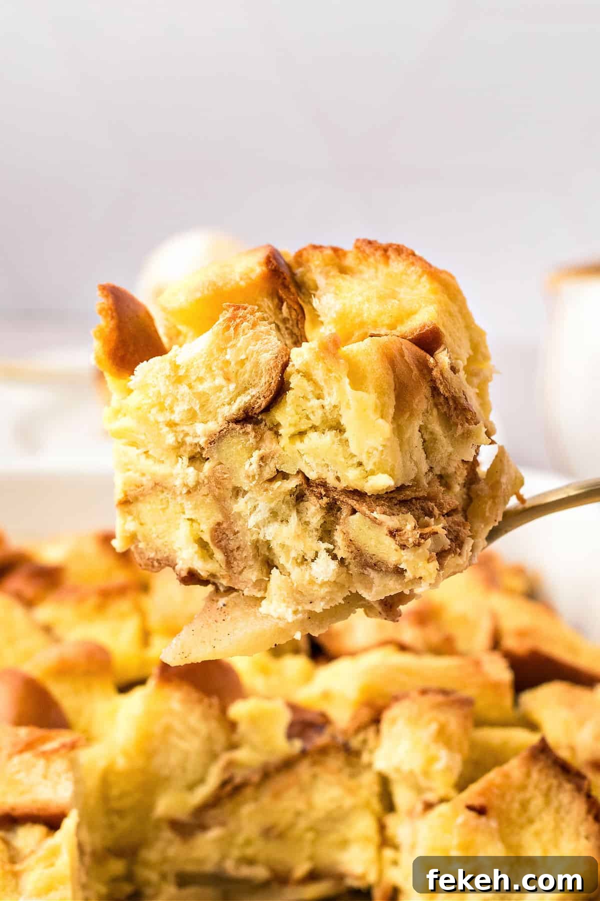 Lifting a serving of apple bread pudding from dish. Light gray background.