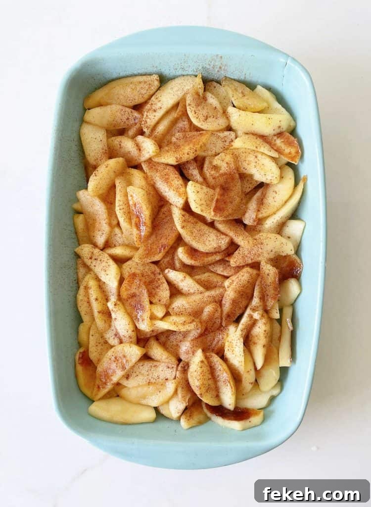 Light blue ceramic dish with cooked apple slices with cinnamon. White surface.