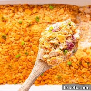 A wooden spoon scoops cheesy Ritz Cracker Chicken Casserole with a golden cracker topping from a white baking dish.