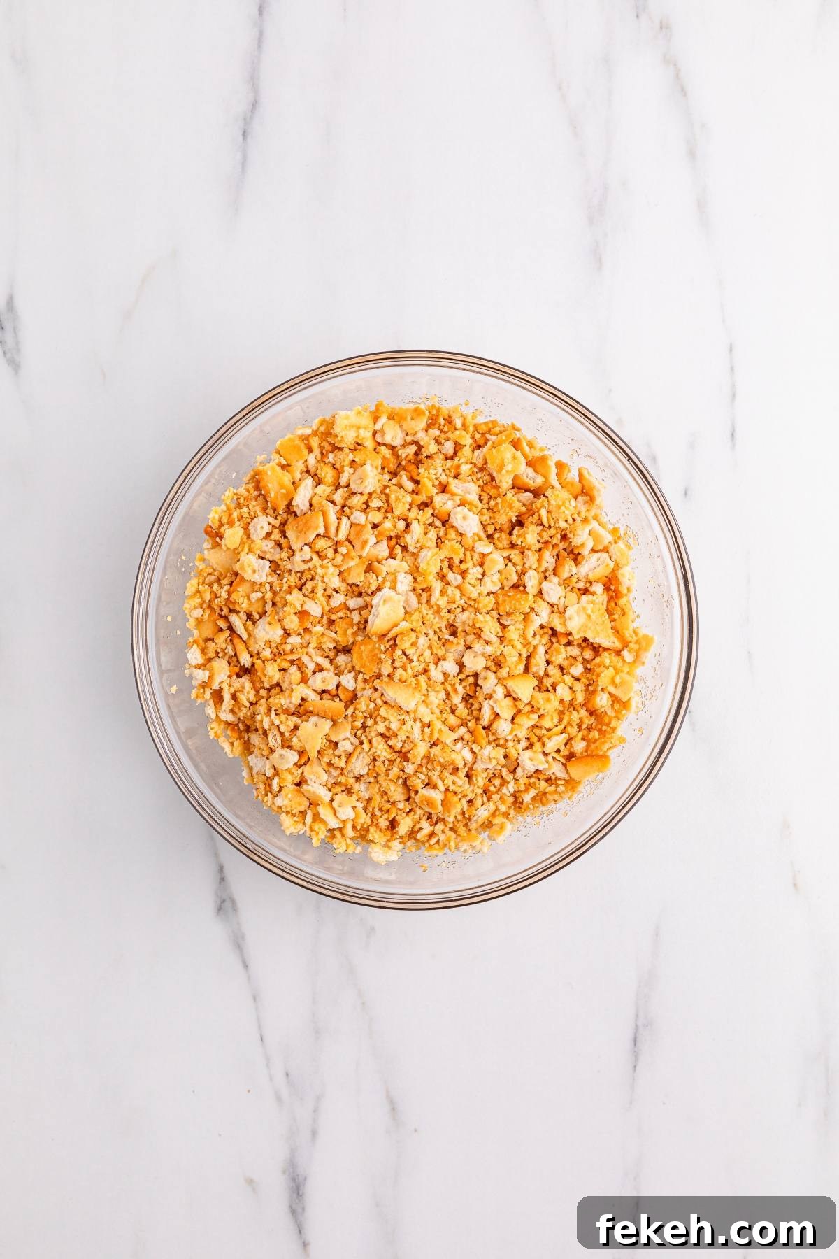 A glass bowl filled with crushed crackers on a white marble surface.