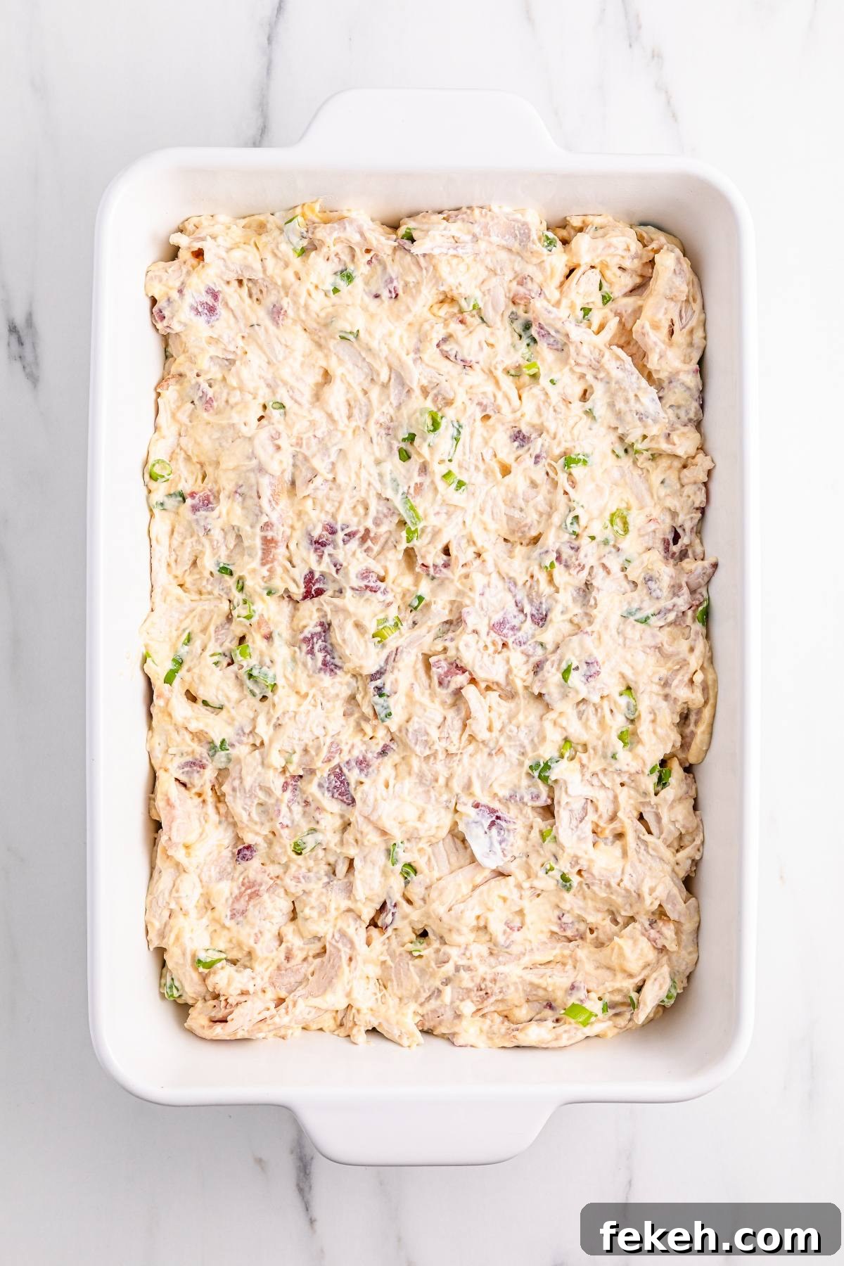 A white baking dish filled with a creamy, mixed casserole topped with chopped green onions.
