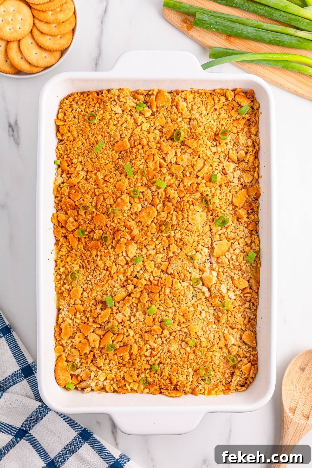 Casserole topped with crushed crackers and green onions in a white dish, with crackers and green onions nearby.