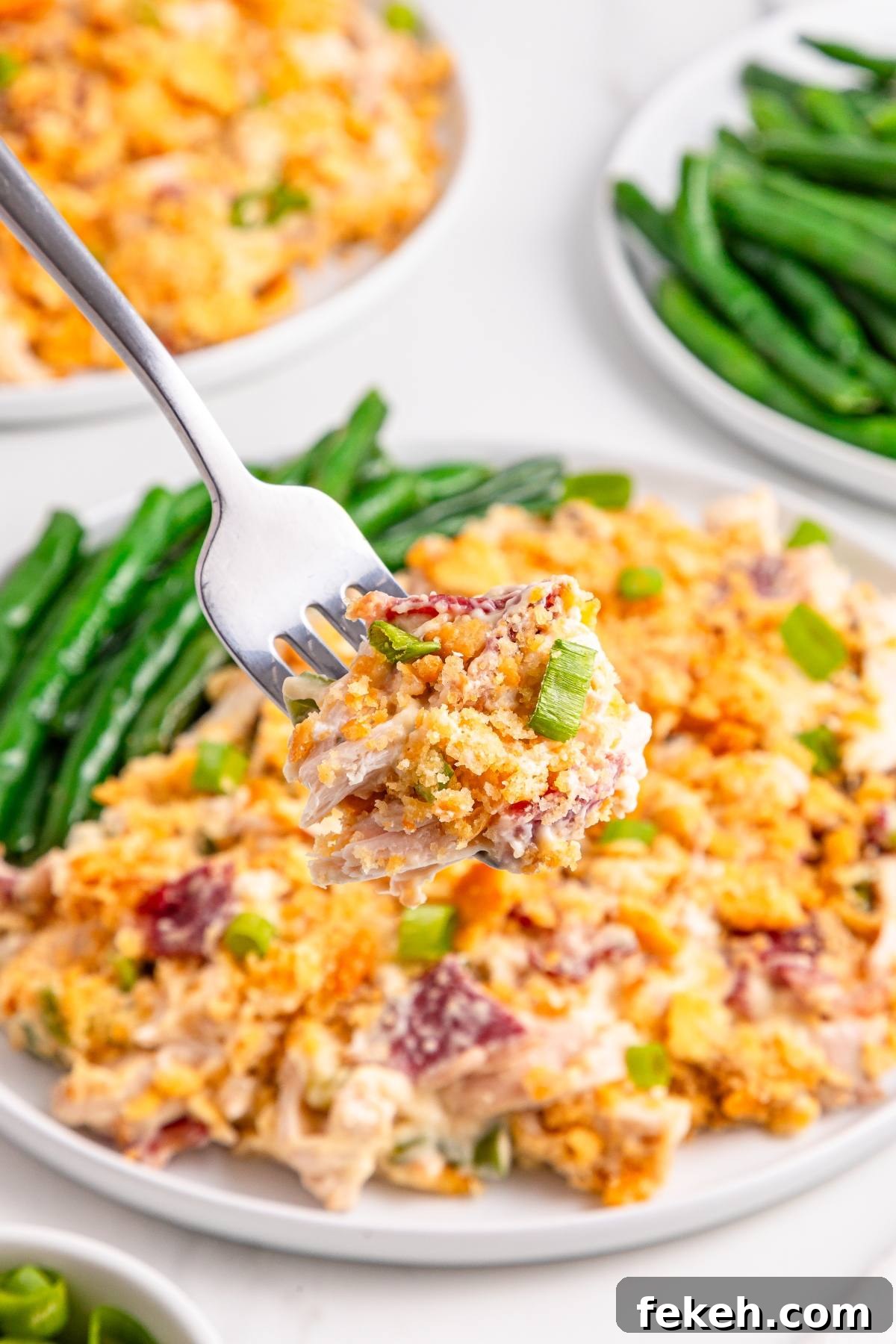 A fork holds a bite of cheesy casserole with green onions above a plate with green beans and more casserole.