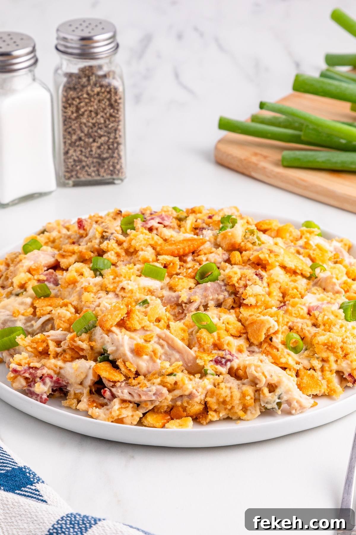 A plate of creamy chicken casserole topped with crumbled crackers and sliced green onions sits on a table.