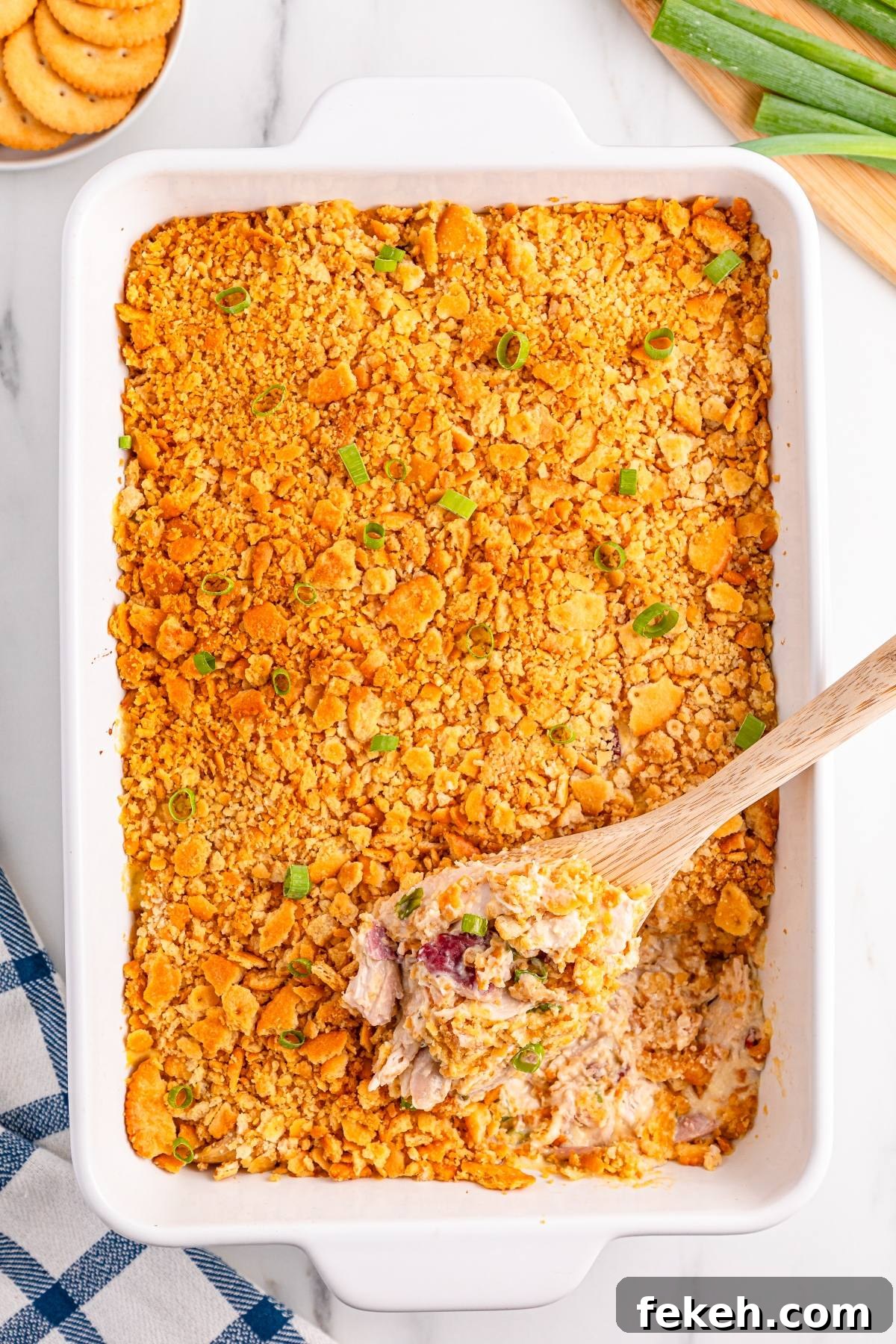 A baked casserole with a golden crumb topping, served in a white dish with a wooden spoon scooping some out.