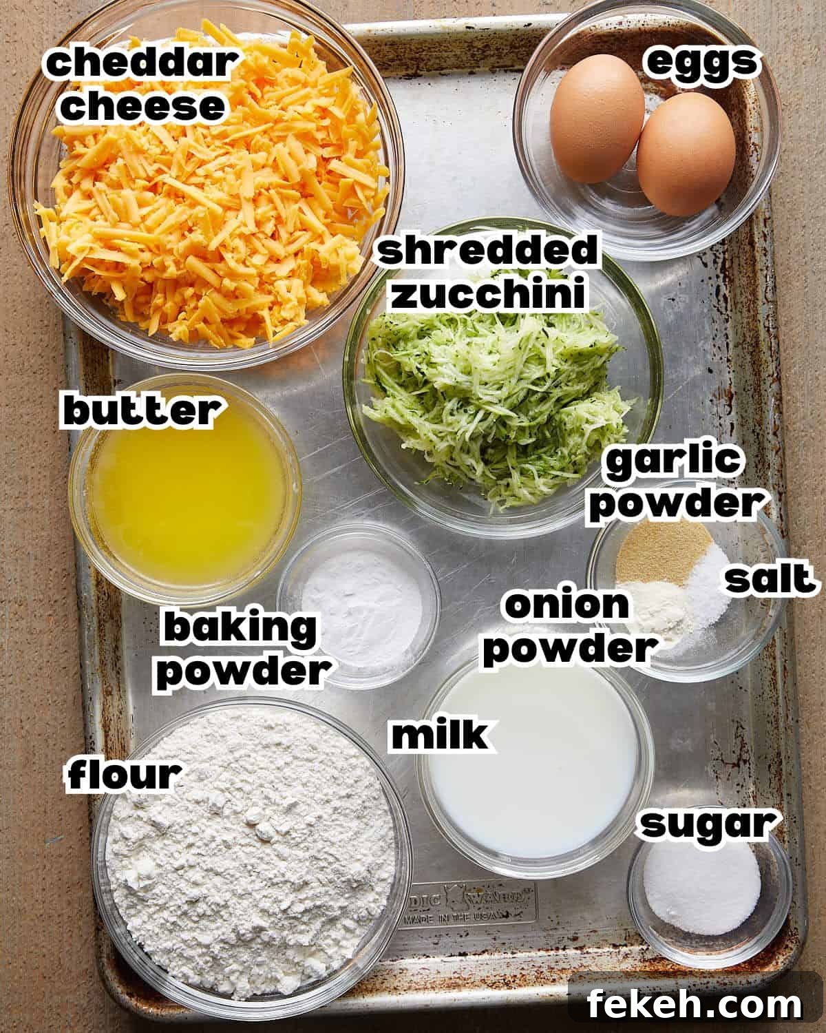 Overhead image of ingredients needed to make savory zucchini muffins on baking sheet. 