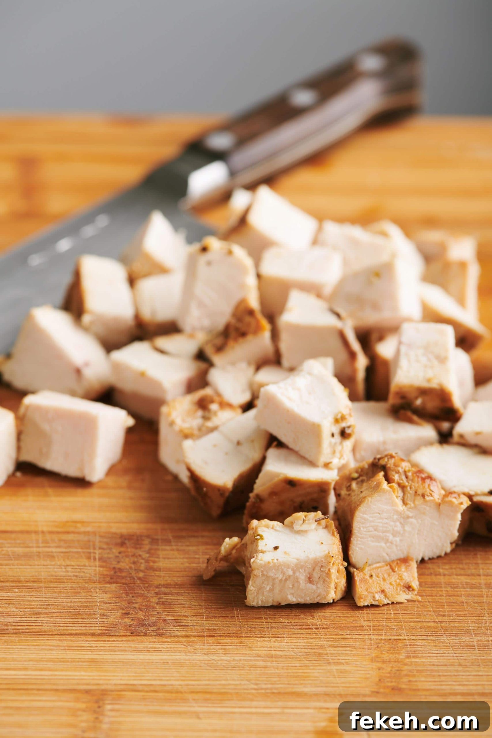 Cubed cooked chicken breast on a cutting board with a knife.