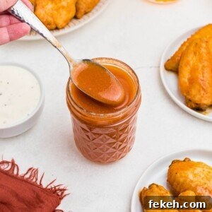 Orange sauce in a small jar, being spooned out, in front of plates of chicken wings.