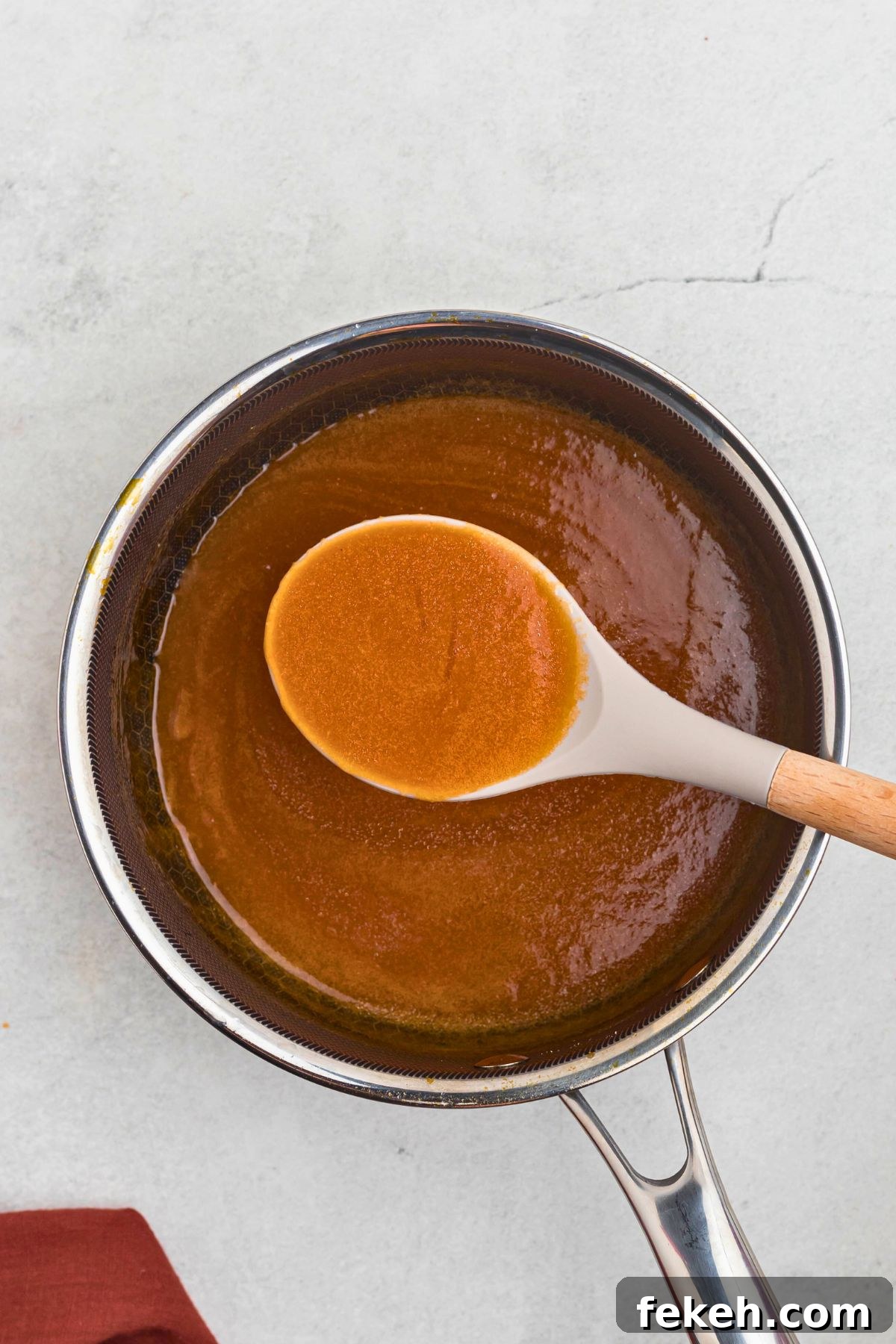 Creamy and buttery sauce in a saucepan, thickening after it's cooled, being spooned up with a serving spoon. 