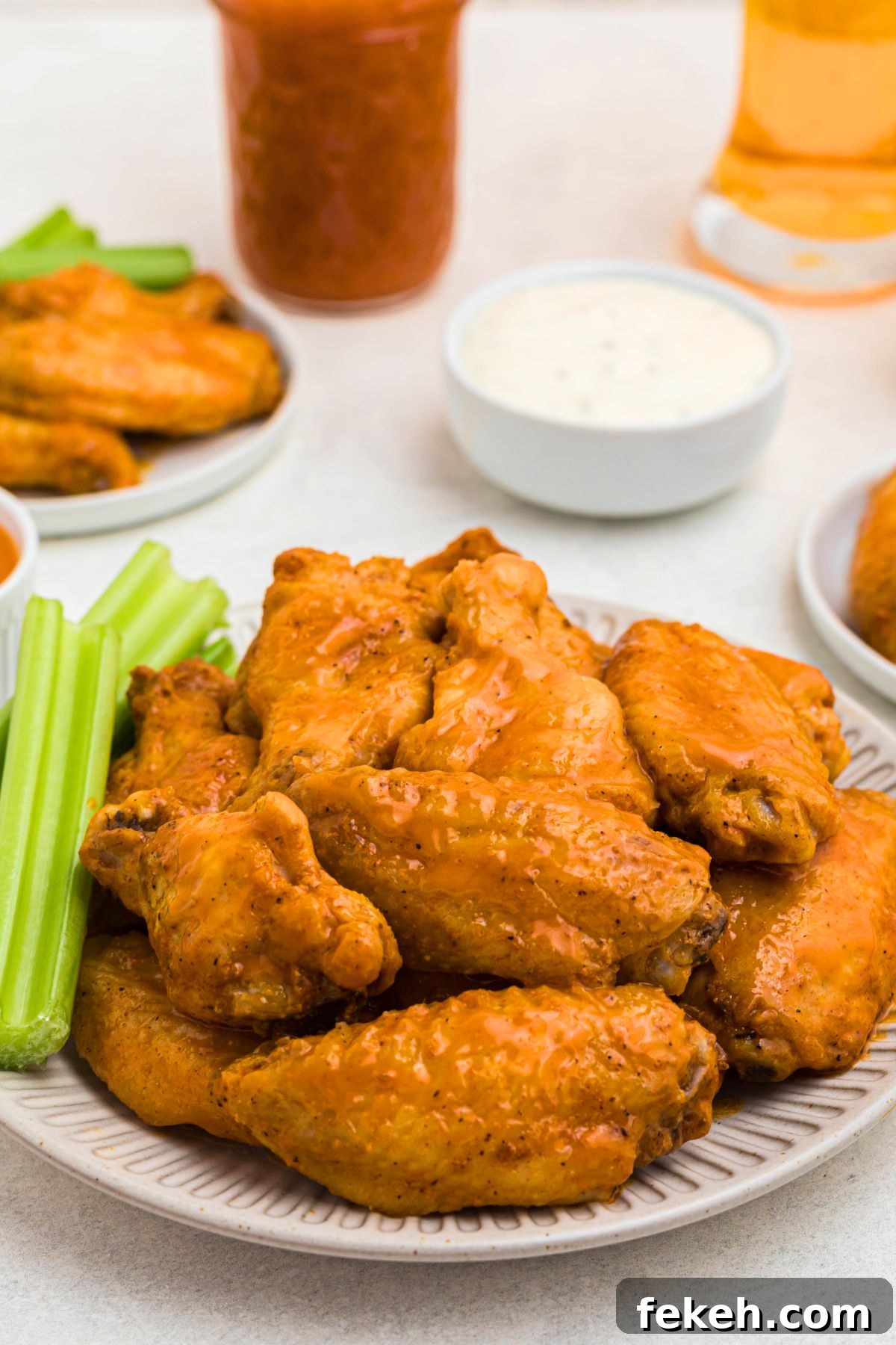 Crispy baked chicken wings, tossed in buffalo sauce, on a white plate with celery sticks on the plate.