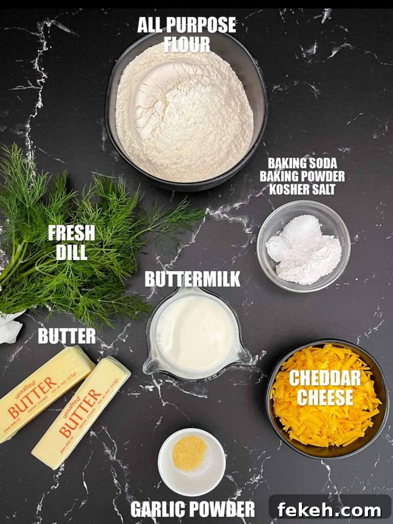 Ingredients for cheddar dill biscuits including flour, shredded cheddar cheese, fresh dill, buttermilk, butter, baking powder, baking soda, kosher salt, garlic powder, and butter for the topping.